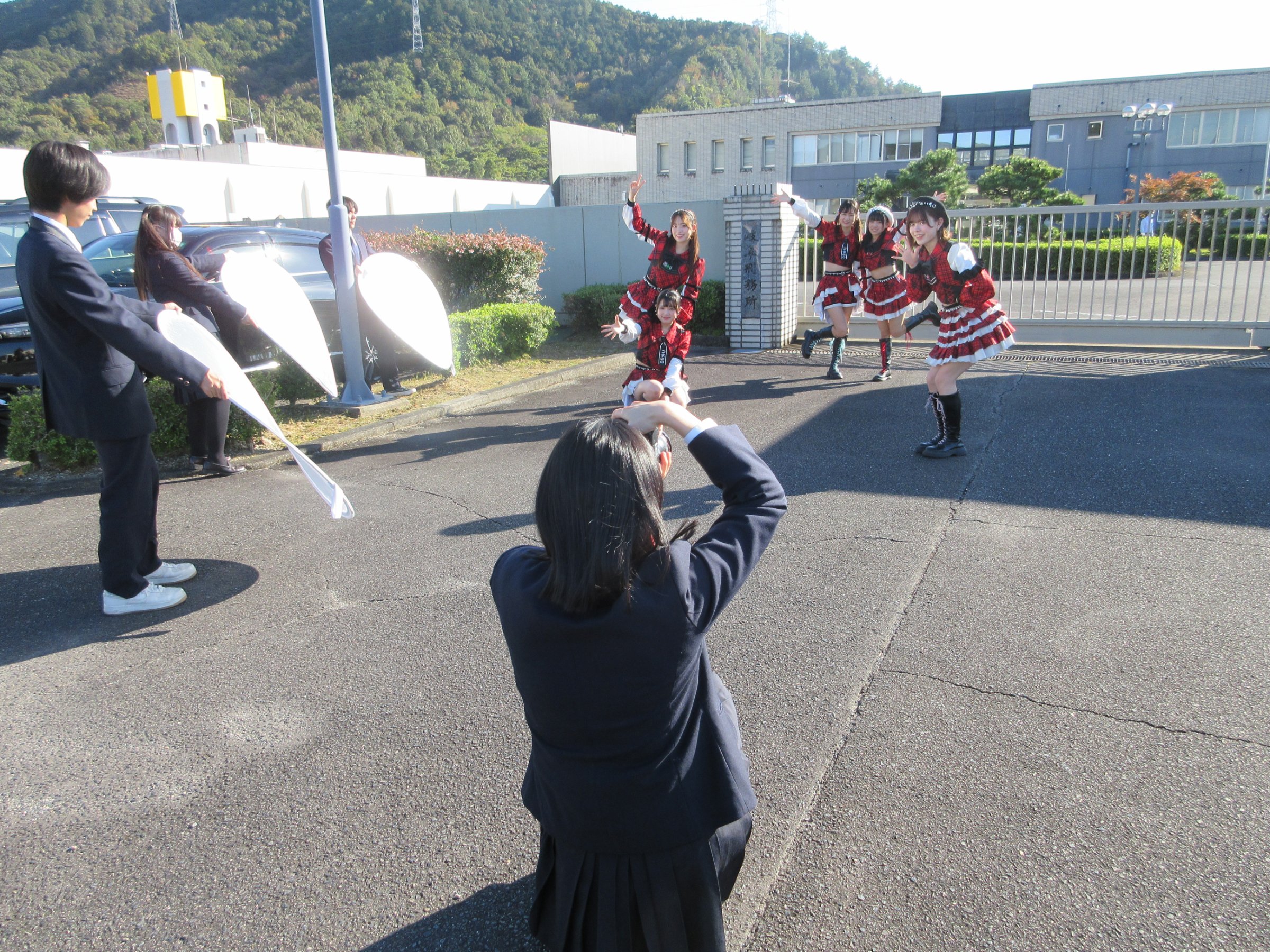 刑務所の前でパフォーマンスするアイドルグループと撮影する高校生